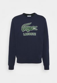 Tmavě modrá mikina z bavlny s vyšitým zeleným krokodýlím logem a nápisem "LACOSTE" na přední straně. Klasický design s kulatým výstřihem.