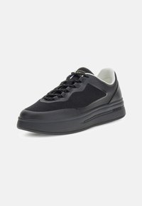Sneaker basse noire avec semelle épaisse, tige en mesh et cuir, lacets noirs à motifs, doublure intérieure blanche et logo "GUESS" sur le côté de la semelle.