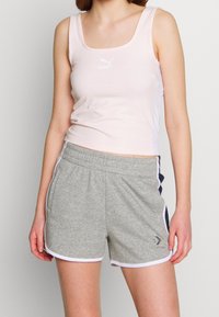 Camiseta sin mangas de color rosa claro con escote cuadrado, combinada con pantalones cortos grises con ribete blanco y detalles laterales.