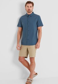 Short-sleeve, collared shirt in dark blue, paired with beige shorts. Sandals feature a brown textured strap and buckle accents.
