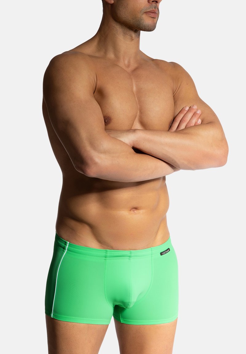 Zelené plavky s hladkou, elastickou texturou. Mají těsný střih a bílé akcentní steh. Obsahují malé logo na pase.