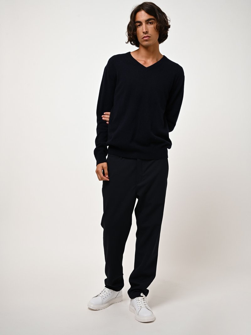 Marineblaues V-Ausschnitt-Pullover aus weichem Material, kombiniert mit locker sitzenden schwarzen Hosen und weißen Sneakern. Schlichte, klare Linien mit minimalen Akzenten.