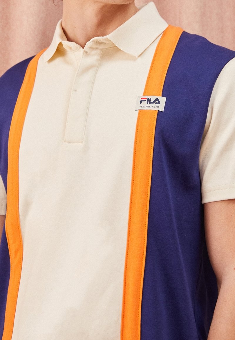 Polo en crème, violet et orange ; en coton ; avec un col et une petite broderie sur la poitrine.