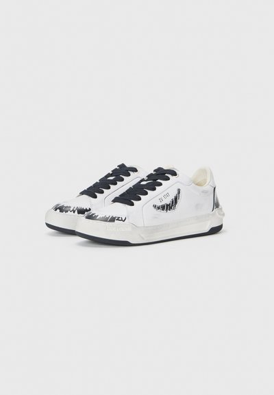 White sneakers with black accents, featuring a patterned design on the toe. Laces are black, and sole design is textured. Branding on the side.