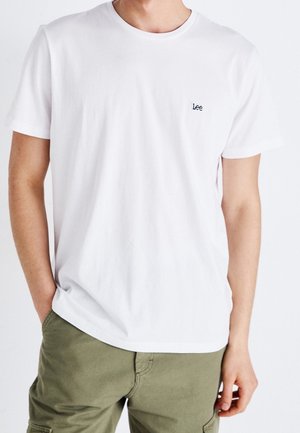 Weisses Baumwoll-T-Shirt mit Rundhalsausschnitt und kurzen Ärmeln. Kleines schwarzes "Lee"-Logo auf der linken Brust. Getragen mit olivgrünen Cargo-Shorts.