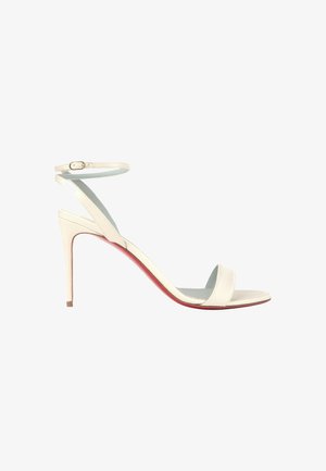 Sandalia blanca de tacón alto con tiras en el tobillo y tacón fino tipo stilettos, vista de lado sobre fondo blanco.