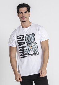 Camiseta blanca de algodón con un gráfico de un oso con una cadena, texto negro que dice "GIANNI KAVANAGH" en el lado izquierdo.