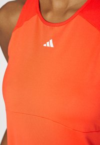 Rode sportieve singlet met een gladde textuur, voorzien van een wit logo op de borst en contrasterend rode stiksels op de schouders.