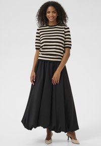 Top en tricot rayé crème et noir avec des manches courtes, associé à une jupe noire fluide ; présente une taille froncée et un tissu doux.
