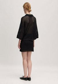 Schwarzes Strickset mit einem lockeren, offen gewebten Oberteil und einem passenden Rock. Beide Teile haben ein strukturiertes Muster und einen entspannten Schnitt.