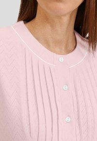 Top de punto en rosa claro con un patrón de chevron texturizado, cuello redondo con ribete blanco y cierres de botones blancos en la parte delantera.