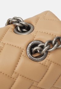 Borsa in pelle trapuntata beige con hardware in tonalità argento a catena e anello. La superficie presenta una texture liscia con dettagli di cucitura precisi.
