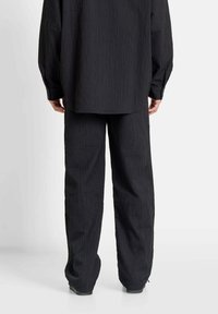 Zwart textuur shirt en broekset, met verticale strepen, losse pasvorm, knoopdetails op de mouwen en rechte broekspijpen.