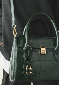 Crocodile-embossed dark green handbag with a gold clasp and lock detail, short handles, and a detachable shoulder strap.
