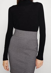 Top noir à col roulé associé à une jupe taille haute avec un motif pied-de-poule noir et blanc. Tissu lisse avec une silhouette ajustée.