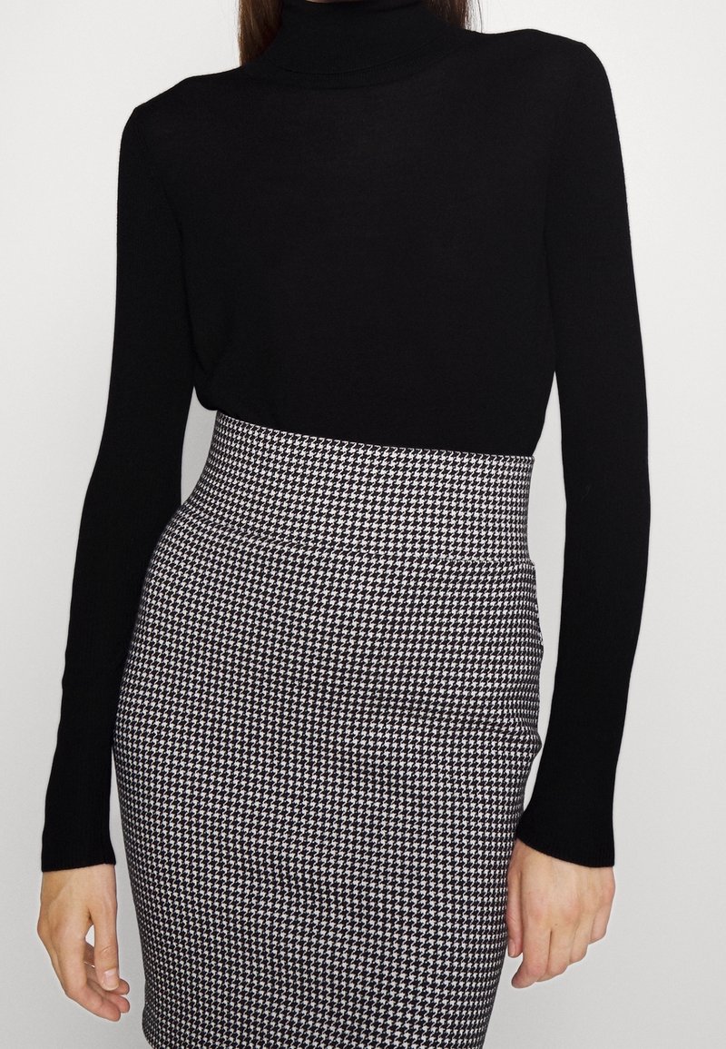 Top noir à col roulé associé à une jupe taille haute avec un motif pied-de-poule noir et blanc. Tissu lisse avec une silhouette ajustée.