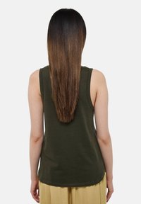 Haut sans manches vert en coton doux, avec un ourlet arrondi et une coupe décontractée. La vue arrière montre des cheveux bruns lisses et droits retombant.