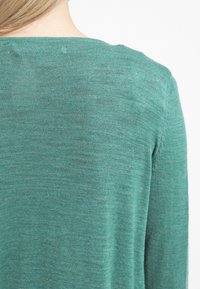 Vihreä villapaita, jossa on pyöreä pääntie ja pitkät hihat. Kankaassa on sileä rakenne ja hienovarainen, epätasainen neulekuvio.