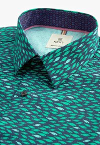 Camicia a maniche corte realizzata in un tessuto blu scuro con un motivo a pesci in diverse tonalità di verde. Include un colletto interno a contrasto con motivo.