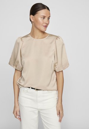 Beige Satinbluse mit kurzen Puffärmeln, rundem Ausschnitt und lässiger Passform. Kombiniert mit weißen Jeans und einem schwarzen Gürtel.