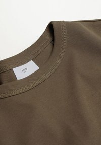 T-shirt vert olive avec un col rond, fabriqué en coton doux, présentant une légère texture côtelée et une étiquette cousue à l'intérieur du col.