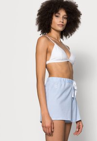 Vit triangulär bikiniöverdel och ljusblå randiga shorts med elastisk midja och vit dragsko. Tyget ser slätt ut.