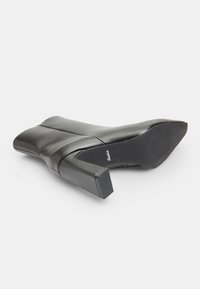 Black leather high-heeled shoe with a square toe and block heel. Smooth texture, with a logo on the insole and a rubberized sole.
