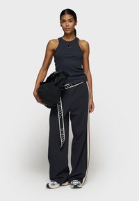 Dunkles Tank-Top mit gerippter Textur, kombiniert mit hochtaillierten schwarzen Hosen mit Seiteneinsätzen und einem Gürtel. Schwarze Tasche mit weichem Finish.