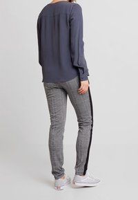 Grå långärmad blus med en slät textur, kombinerad med byxor i slim fit med rutmönster som har en svart sidremsa och vita sneakers.