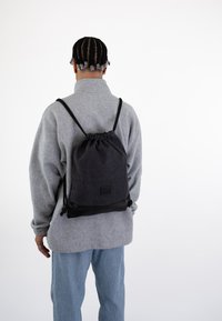 Piilopussinauhalla varustettu tummanharmaa kangas, jonka alaosa on musta, logotarralla, säädettävillä olkahihnoilla ja pehmeällä pinnalla.