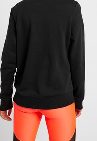 Felpa nera con scollatura a girocollo e orlo a coste, abbinata a leggings arancioni chiari a vita alta con dettagli neri.