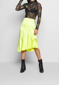 Musta pitkähihainen verkkopaita, jossa on vihreitä taivaankappaleita, yhdistetty kirkkaansiniseen neonkeltaiseen epäsymmetriseen hameeseen. Mustat nilkkurit täydentävät asua.