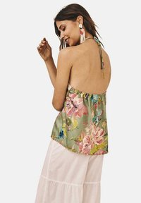 Top halter floral en verde con flores rosas y azules; tejido ligero, corte suelto y tirantes ajustables al cuello. Falda blanca abajo.