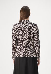 Beige ja musta zebra-mustriga bleiser. Pikad varrukad, keha vormiv disain ja väike nööbikas detail kaela juures. Näidatud tagantvaade.