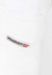 Tessuto denim bianco con un piccolo tag sulla tasca che presenta "Diesel Industry" in grigio e rosso, mostrando i dettagli e il logo del marchio.