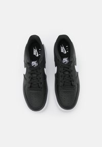 Črne superge Nike Air Force 1 z zgornjim delom iz teksturirane usnjene tkanine, belim znakom Swoosh, črnimi vezalkami in belim gumijastim podplatom.