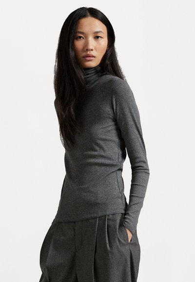 Grå turtleneck genser i strukturert ribbestrikk med lange ermer, tettsittende design og sideåpninger. Brukt sammen med mørke plissert bukser.