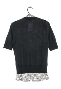 Black knit sweater with short sleeves, ribbed cuffs, and a floral-patterned fabric peeking from the bottom hem. Hangs on a hanger.