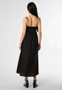 Schwarzes Maxikleid mit dünnen verstellbaren Trägern, gerafftem Oberteil, schwingendem Rock und glatter Textur. Getragen mit Blockabsatzsandalen.