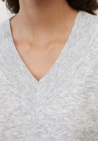 Maglione grigio chiaro a scollo a V con dettagli a coste attorno al colletto; texture morbida; cuciture visibili. Inquadratura ravvicinata che mette in risalto il colletto.