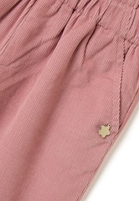 Roze corduroy broek met elastische tailleband en een kleine gouden vierbladige klavertje charm nabij de zak.
