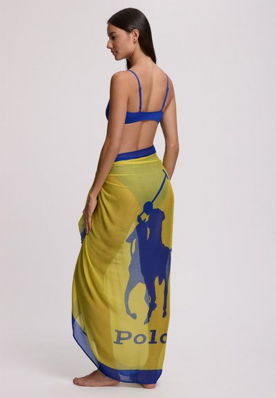 Haut de bikini bleu associé à un paréo jaune transparent avec une grande silhouette de joueur de polo bleue et le texte "Polo" le long de l'ourlet.