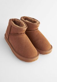 Bruna mockasiner med mjukt pälsfoder, rund tå och gummisula. Sömnadsdetaljer längs sömmarna och slip-on design.