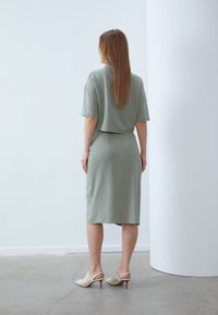 Svetlozelený dvojdielny outfit pozostávajúci z voľného topu s krátkym rukávom a sukne po kolená. Modelka má na sebe béžové sandále na podpätku.
