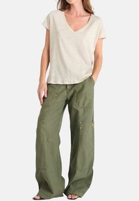 Camiseta de manga corta color beige con escote en v, combinada con pantalones cargo holgados en color oliva que presentan bolsillos laterales y detalles de botones dorados. Estilo casual, ajuste relajado.