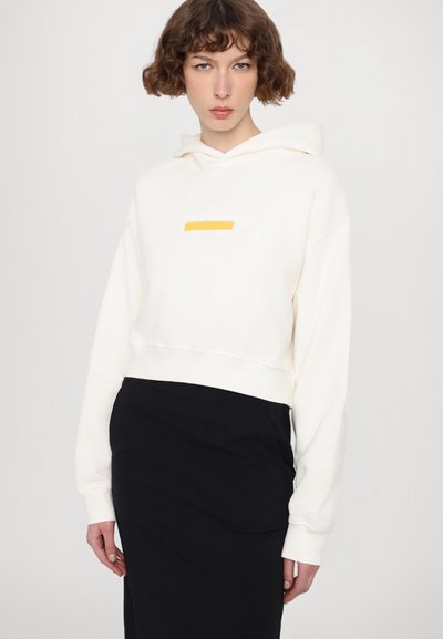 Haut court blanc en matériau doux, avec un logo en front et une touche de jaune. Associé à une jupe noire ajustée.
