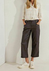 Zwarte cropped broeken met een gladde textuur, voorkeurszakken en een knoop aan de taille. Gecombineerd met een geruit overhemd met knopen en witte sneakers.