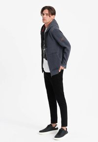 Felpa navy con zip frontale, cordini regolabili, tasche laterali e fodera a scacchi. Abbinata a pantaloni neri slim-fit e sneaker nere.