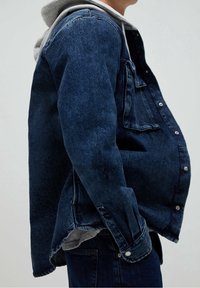 Denimjacka i mörkblått med grå huva, med en framficka, knapplåsning och avslappnad passform. Slät textur och skräddarsydd silhuett.