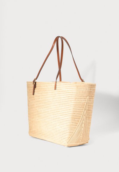 Sac cabas rectangulaire tissé beige avec poignées en cuir marron, présentant un détail triangulaire texturé sur le côté sur un fond uni.